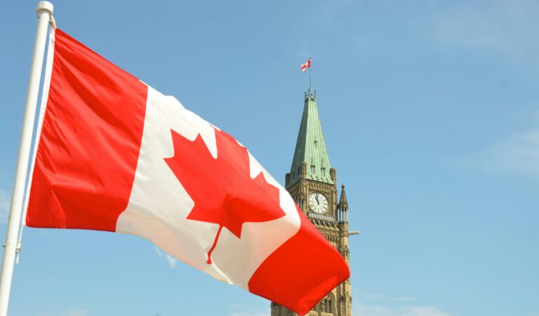 Canadian flag gently blowing in the wind with the parliament buildings in the background.