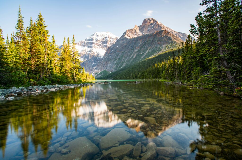 pictured is mount edith cavell in jasper national park, her reflection shimmering on the water flanked by trees.