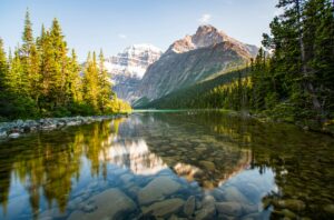 pictured is mount edith cavell in jasper national park, her reflection shimmering on the water flanked by trees.